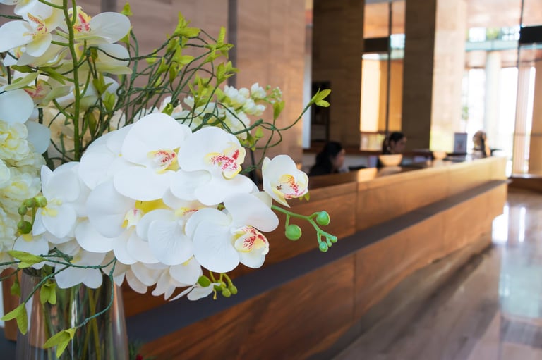 Reception area in luxury hotel close up on flower foreground with receptionist sitting in zen style long wood counter and blur background.