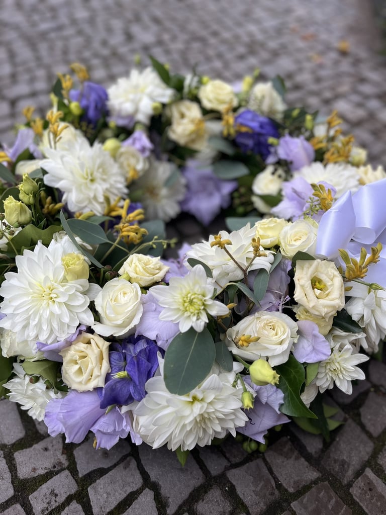 Floral arrangement with white roses and dahlias, purple delphiniums, and eucalyptus leaves on a gray stone surface