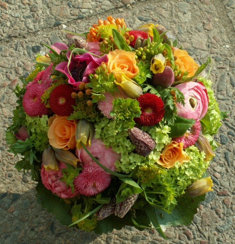 Vibrant floral bouquet with pink gerberas, orange roses, yellow flowers, and green foliage on gray stone background