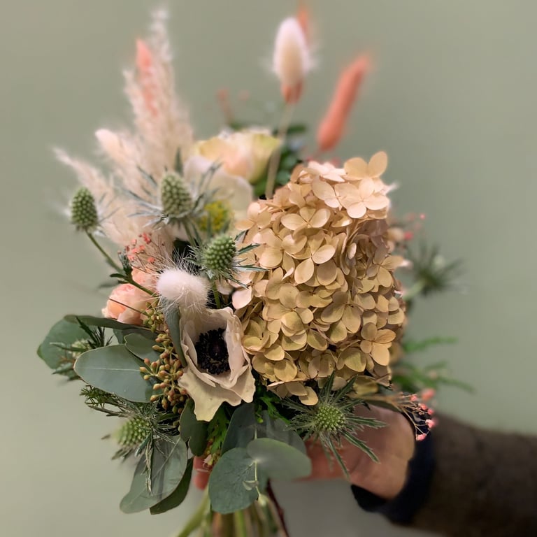 Dried flower bouquet with tan hydrangeas, pink proteas, green seed pods, and eucalyptus greenery held in a vase