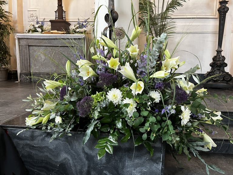 Large floral arrangement with white and purple flowers in a black container inside a formal interior space