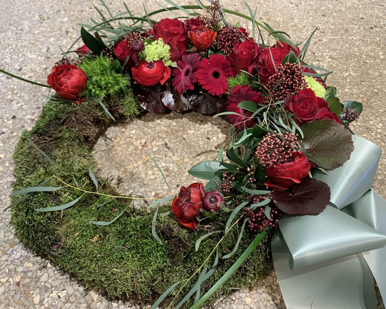Moss wreath with deep red roses, burgundy gerberas, and green chrysanthemums, tied with a silver ribbon
