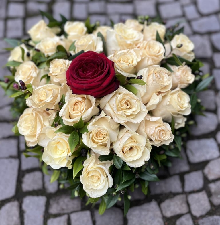Heart-shaped floral arrangement with cream roses and one red rose in the center on a gray stone background