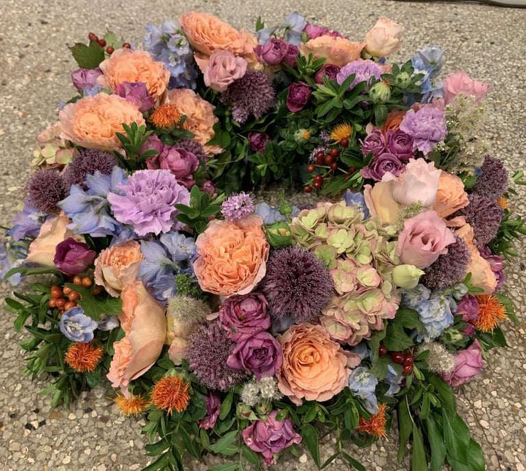 Colorful floral arrangement with peach roses, purple dahlias, pink carnations, and orange mums on a concrete surface