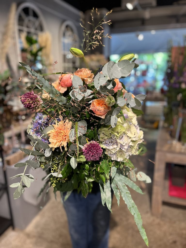 Lebendige Blumenarrangement mit pfirsichfarbenen Dahlien und weißen Hortensien in einer blauen Vase