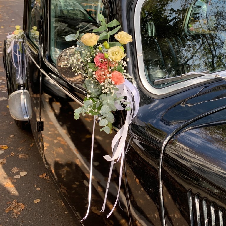 Black vintage car decorated with yellow, pink, and white flowers and ribbons for a wedding