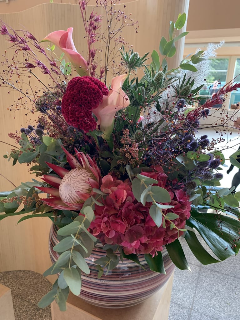 A colorful floral arrangement with deep red and pink flowers, purple berries, and green foliage in a striped ceramic vase