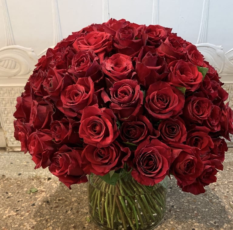 Large bouquet of deep red roses in a clear glass vase with green stems on a marble surface